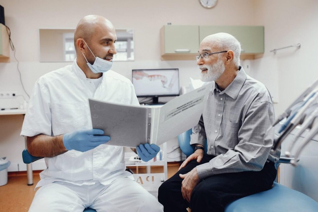 Dentist and elderly patient seated in a dental chair, engaged in a conversation.