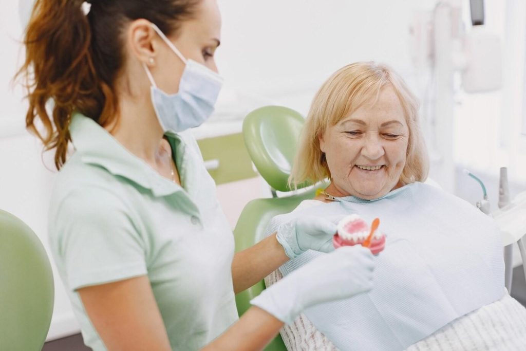 an old lady observing the doctor cleaning fake teeth.